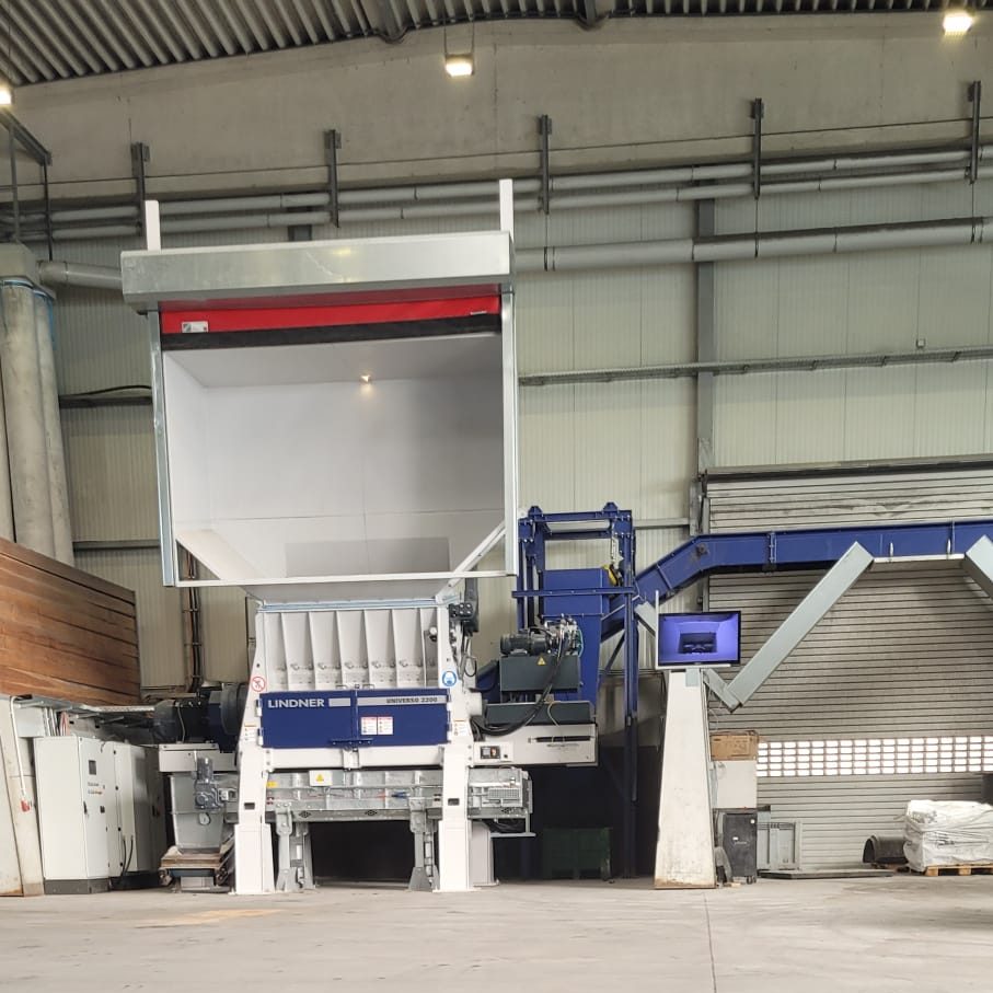 Industrial press with a large hopper in a factory, blue-and-white Lindner machine under a high ceiling