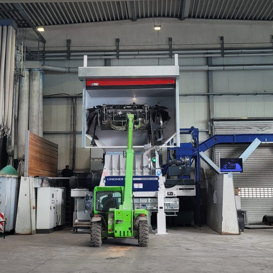 Green telehandler lifts a large industrial machine onto a raised platform inside a spacious workshop.